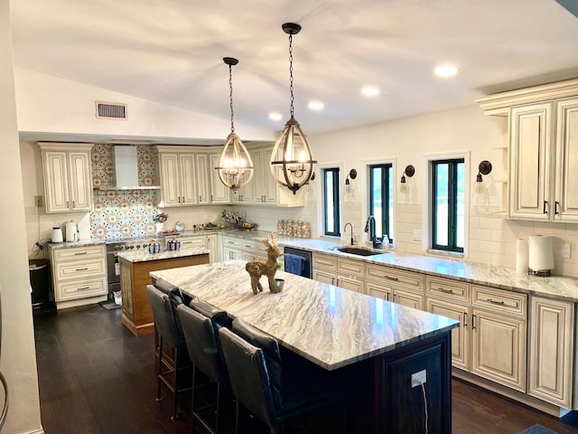 kitchen with light stone countertops, sink, wall chimney exhaust hood, kitchen peninsula, and a kitchen island