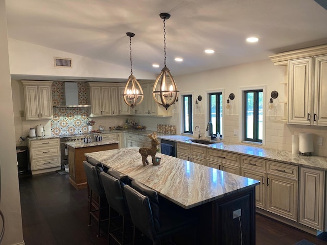 kitchen featuring light stone countertops, a center island, wall chimney range hood, and sink