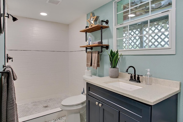 bathroom with tiled shower, vanity, and toilet