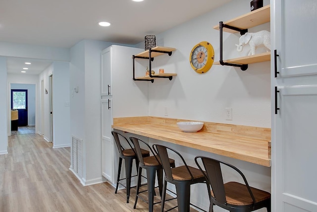 kitchen featuring a kitchen breakfast bar, white cabinetry, butcher block countertops, and light wood-type flooring