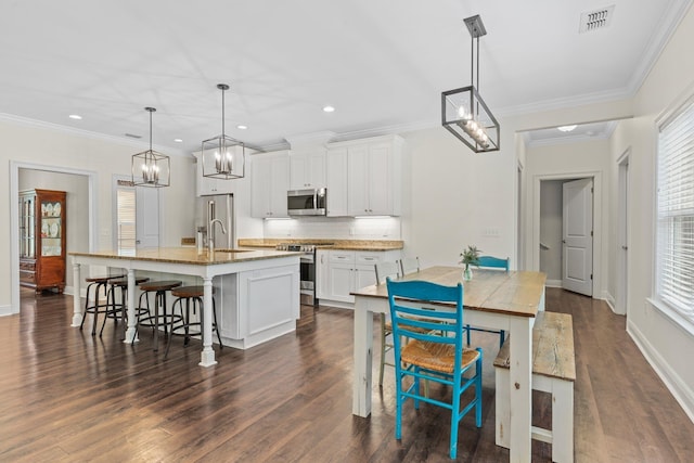 kitchen with a breakfast bar area, visible vents, appliances with stainless steel finishes, white cabinets, and an island with sink