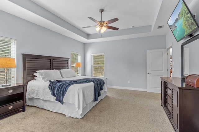 bedroom featuring ceiling fan, light carpet, visible vents, baseboards, and a raised ceiling