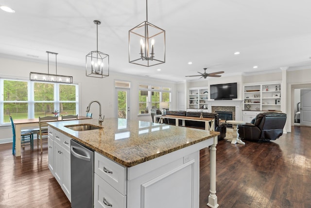 kitchen with an island with sink, decorative light fixtures, light stone countertops, white cabinetry, and a sink