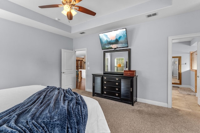 carpeted bedroom featuring a ceiling fan, baseboards, visible vents, and a tray ceiling