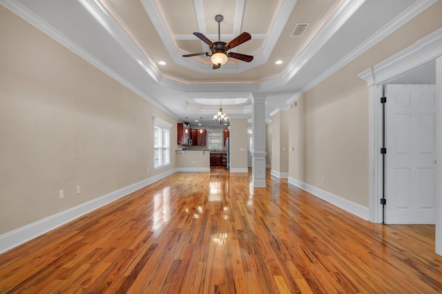 unfurnished living room with ceiling fan with notable chandelier, light wood-type flooring, ornamental molding, a tray ceiling, and decorative columns