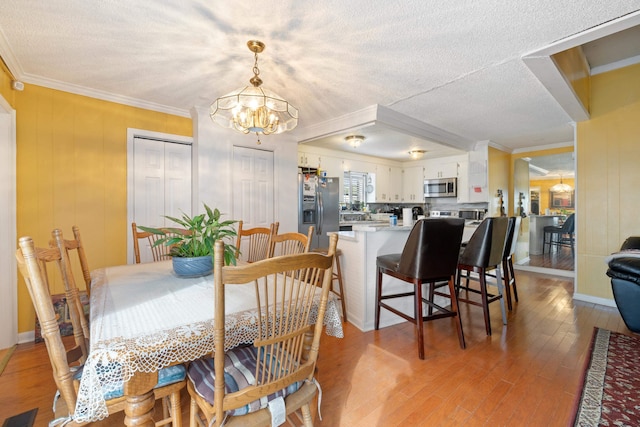 dining space featuring crown molding, a textured ceiling, a notable chandelier, and light wood-type flooring