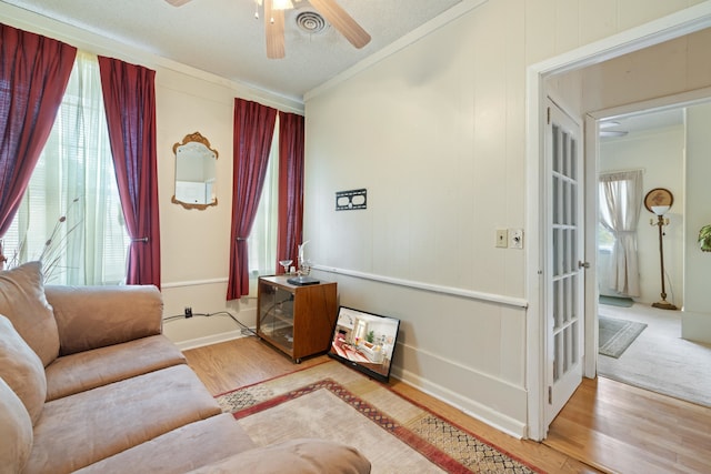 living room featuring crown molding, ceiling fan, light hardwood / wood-style floors, and a textured ceiling