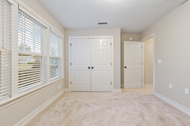 unfurnished bedroom featuring light carpet, a closet, visible vents, and baseboards