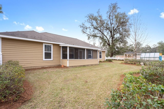 rear view of property featuring an outdoor structure, a sunroom, a yard, roof with shingles, and an exterior structure