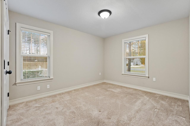 spare room featuring light carpet, plenty of natural light, and baseboards