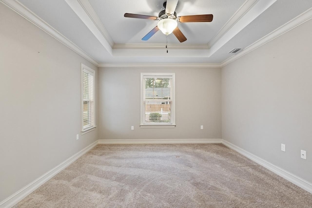 empty room with a tray ceiling, visible vents, ornamental molding, light carpet, and baseboards