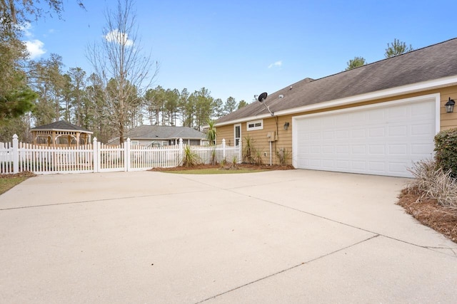 view of side of property featuring a garage, fence, concrete driveway, and a gazebo