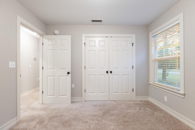 unfurnished bedroom with a closet, light colored carpet, visible vents, and baseboards