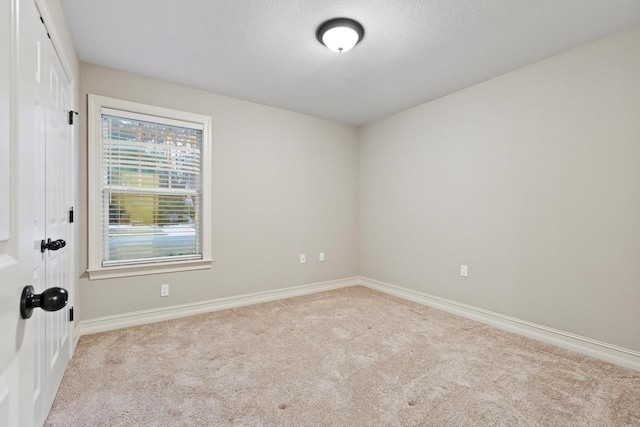 empty room with light carpet, a textured ceiling, and baseboards