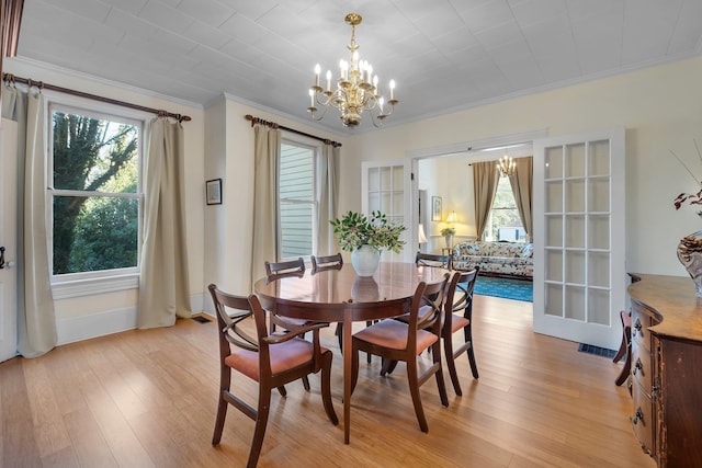 dining space featuring light wood-type flooring, a chandelier, crown molding, and plenty of natural light