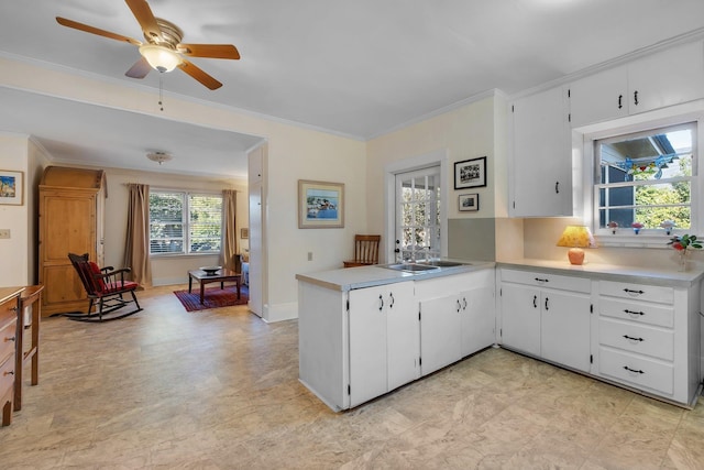 kitchen with ceiling fan, kitchen peninsula, sink, ornamental molding, and white cabinets