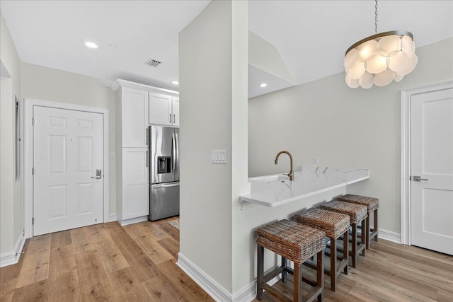 300 S Duval St Unit 2209, Tallahassee, FL 32301 - kitchen with stainless steel fridge, a breakfast bar area, white cabinets, light wood finished floors, and light stone countertops