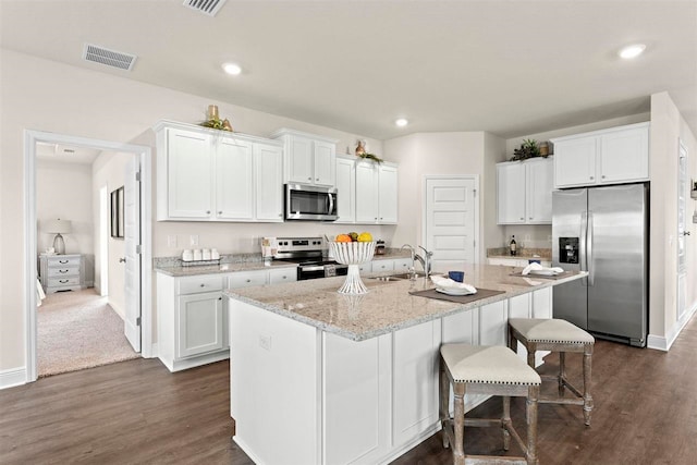 kitchen with light stone counters, a center island with sink, stainless steel appliances, white cabinetry, and dark hardwood / wood-style flooring