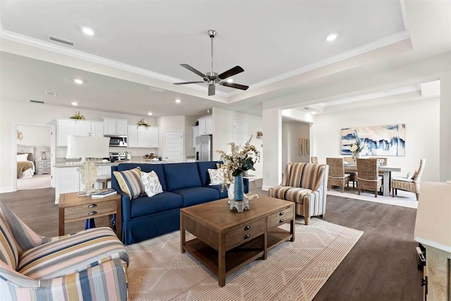 living room featuring ornamental molding, hardwood / wood-style floors, ceiling fan, and a raised ceiling