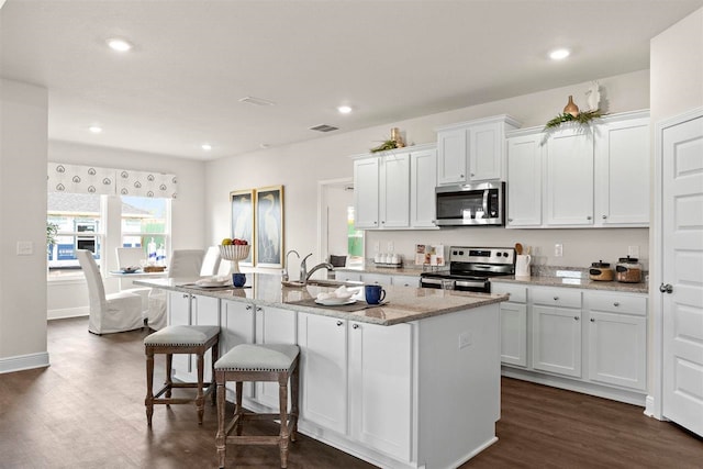 kitchen featuring stainless steel appliances, dark hardwood / wood-style floors, light stone countertops, an island with sink, and white cabinets