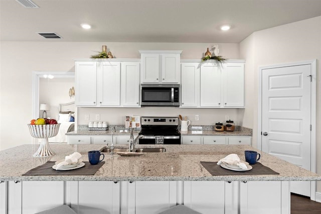 kitchen featuring white cabinetry, a center island with sink, appliances with stainless steel finishes, light stone countertops, and dark hardwood / wood-style floors