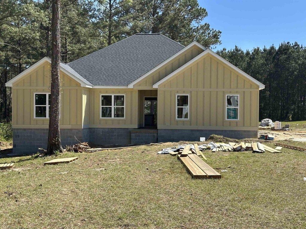 view of front of property with board and batten siding, a front lawn, and roof with shingles