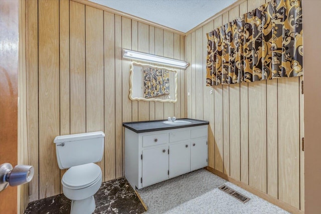 bathroom with wooden walls, vanity, a textured ceiling, and toilet