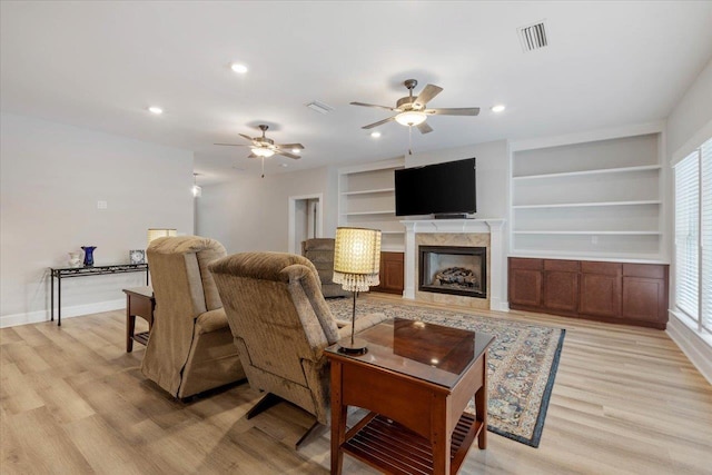 living room featuring light wood-type flooring, built in features, and a premium fireplace