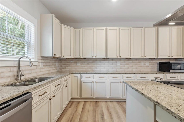 kitchen featuring decorative backsplash, light wood-type flooring, light stone counters, sink, and dishwasher