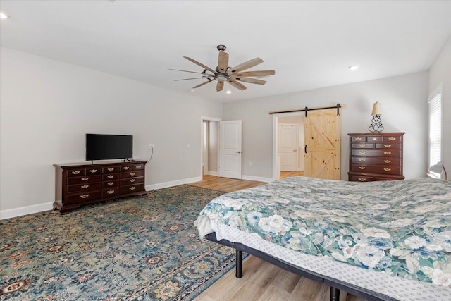 bedroom with hardwood / wood-style floors, a barn door, and ceiling fan