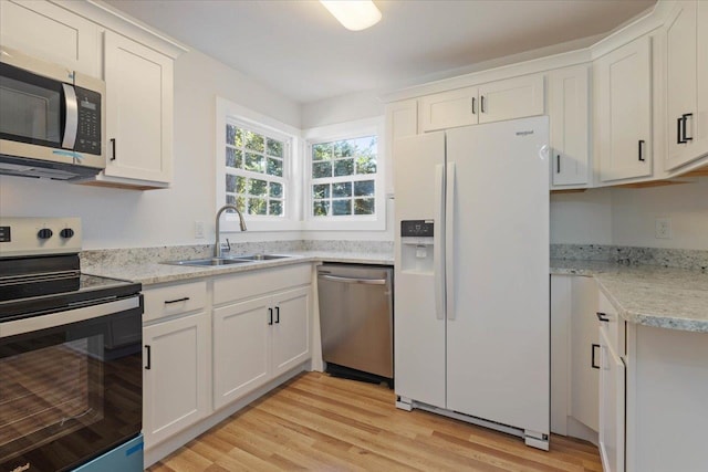 kitchen with appliances with stainless steel finishes, light stone countertops, sink, white cabinets, and light hardwood / wood-style flooring