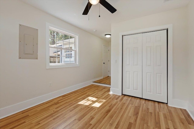 unfurnished bedroom featuring electric panel, light hardwood / wood-style floors, ceiling fan, and a closet