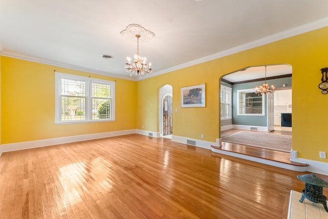unfurnished living room with crown molding, an inviting chandelier, arched walkways, visible vents, and wood finished floors