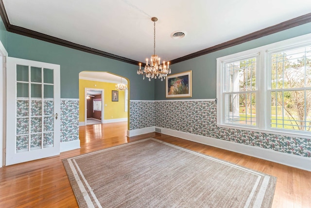 empty room featuring a notable chandelier, wood finished floors, visible vents, wallpapered walls, and arched walkways