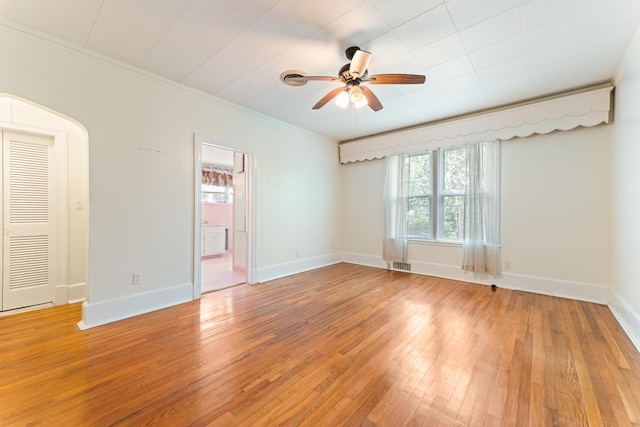 empty room featuring crown molding, light wood-type flooring, baseboards, visible vents, and ceiling fan