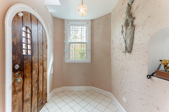 entryway with baseboards, arched walkways, a textured wall, and light tile patterned floors
