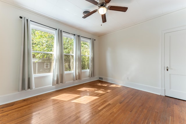 spare room with wood-type flooring, visible vents, baseboards, and ceiling fan