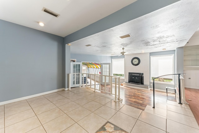 interior space featuring baseboards, tile patterned floors, ceiling fan, visible vents, and a fireplace