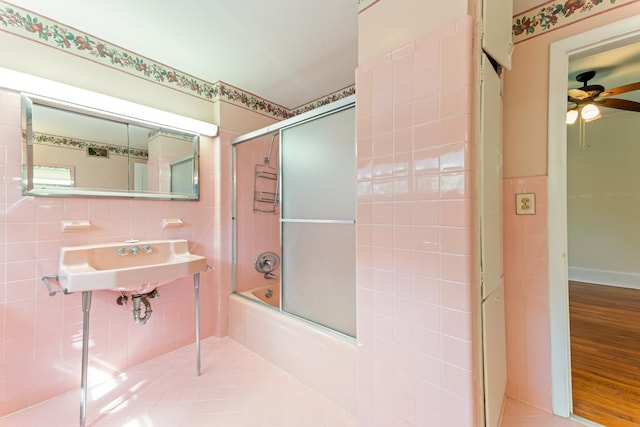 bathroom featuring a sink, bath / shower combo with glass door, tile walls, and a ceiling fan