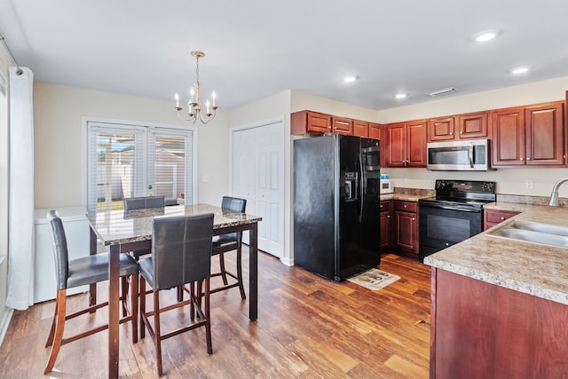 kitchen with pendant lighting, sink, a notable chandelier, black appliances, and light hardwood / wood-style flooring