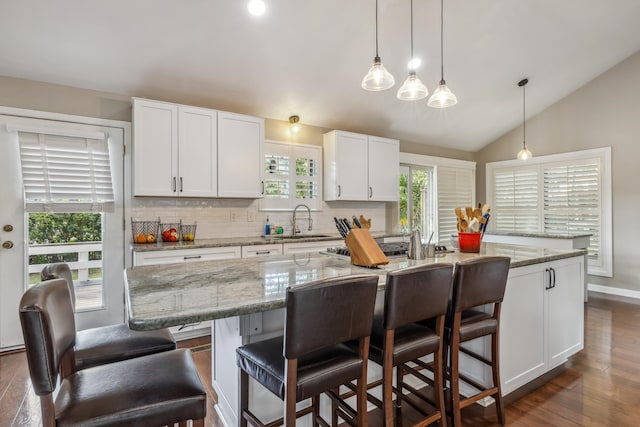 kitchen featuring tasteful backsplash, vaulted ceiling, white cabinets, and a sink