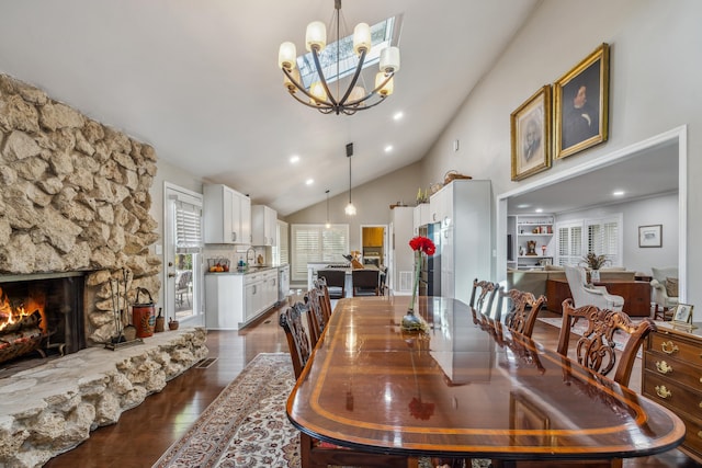 dining space with high vaulted ceiling, recessed lighting, a stone fireplace, dark wood-type flooring, and a notable chandelier