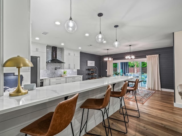 195 Coe Landing Rd, Tallahassee, FL 32310 - kitchen featuring wood finished floors, an inviting chandelier, decorative backsplash, wall chimney range hood, and white cabinets