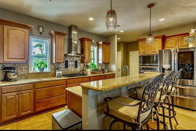 kitchen featuring wall chimney range hood, stainless steel appliances, light stone countertops, and a center island with sink