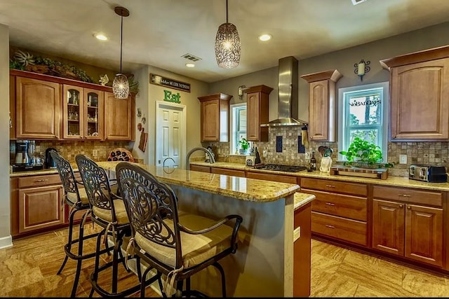 kitchen featuring a kitchen island, light stone countertops, a breakfast bar, and wall chimney exhaust hood