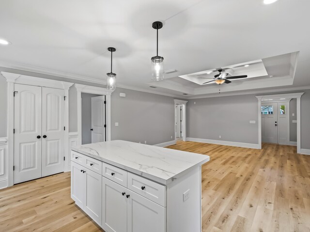 kitchen featuring white cabinets, light hardwood / wood-style floors, ornamental molding, and a tray ceiling