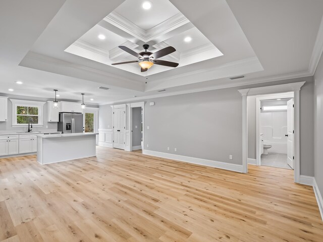 unfurnished living room with sink, ornamental molding, ceiling fan, a tray ceiling, and light wood-type flooring