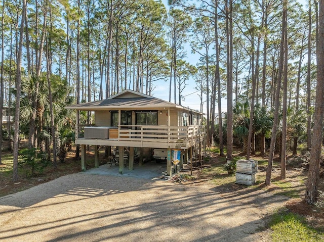 coastal home featuring covered porch, stairway, a carport, roof with shingles, and driveway