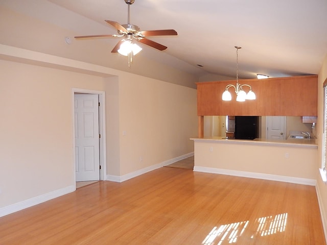 unfurnished living room featuring ceiling fan with notable chandelier, light wood-type flooring, and vaulted ceiling