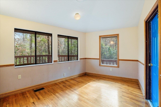 unfurnished room featuring wallpapered walls, baseboards, visible vents, wainscoting, and light wood-style floors